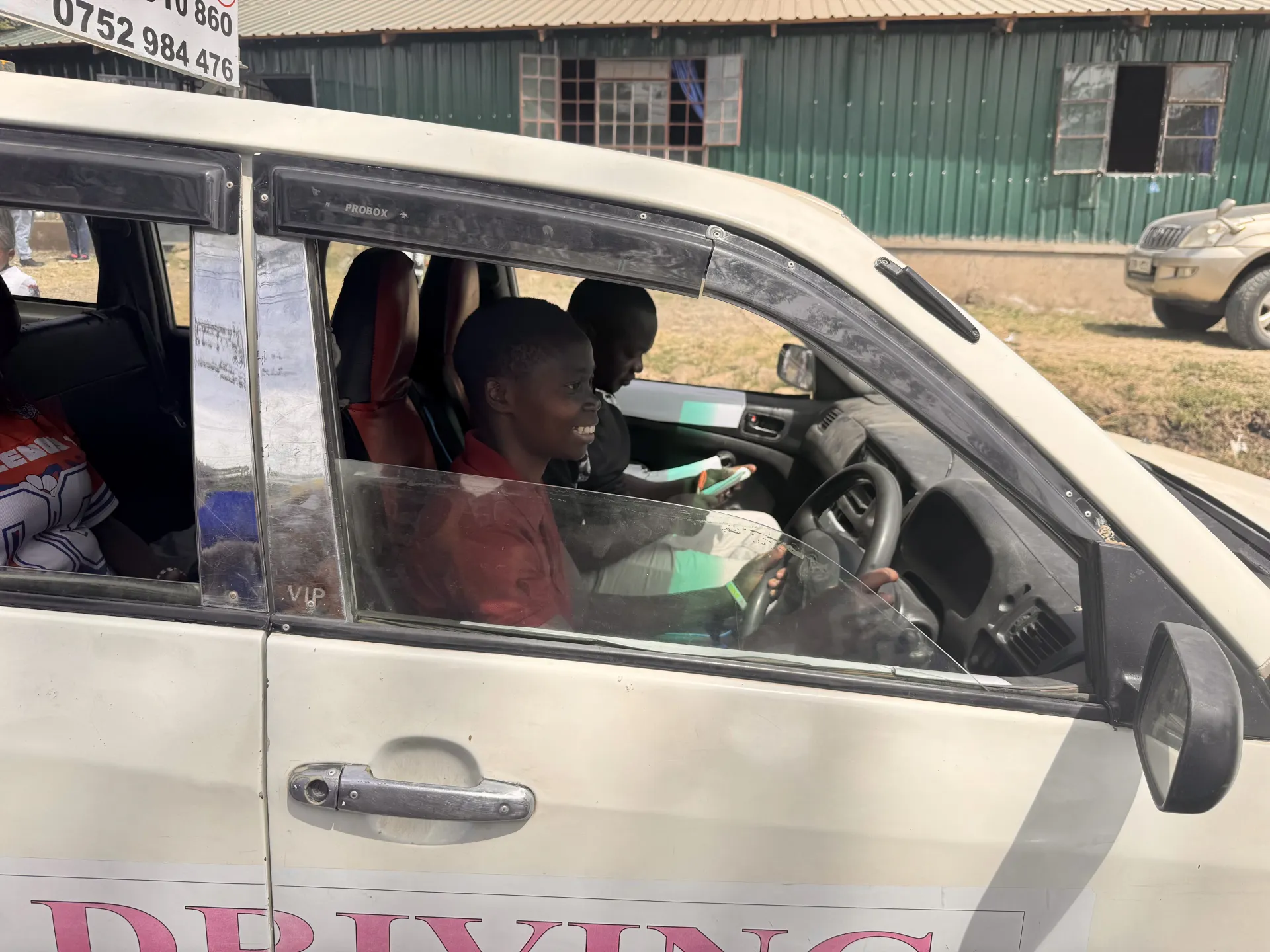 A smiling woman practising driving with an instructor beside her