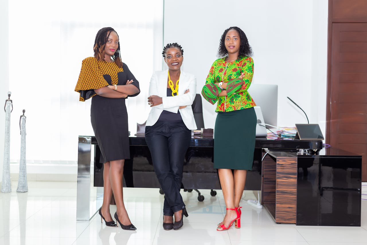 Three African businesswomen posing confidently in a modern office environment showcasing professionalism and style.