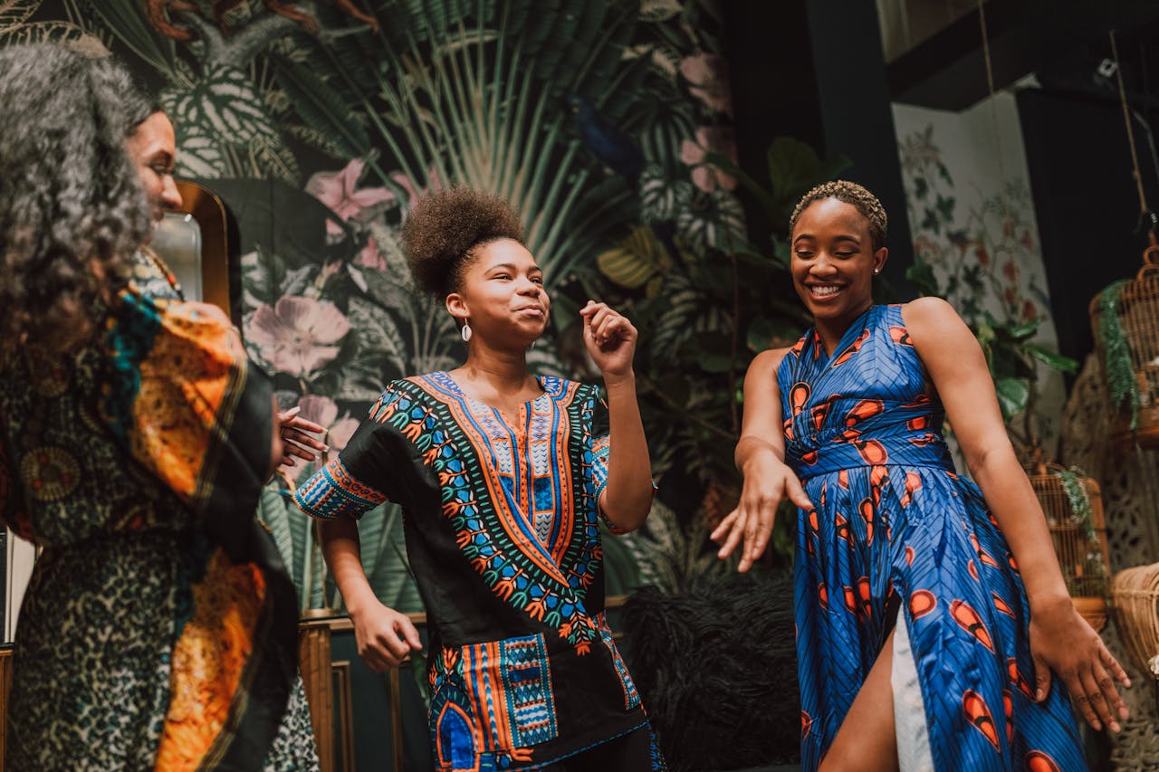 Group of women joyfully dancing in vibrant traditional African attire indoors.